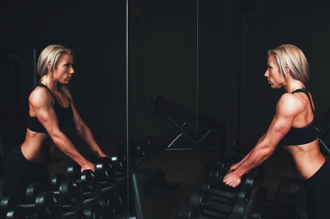 woman wearing black top holding black dumbbells standing in front of mirror