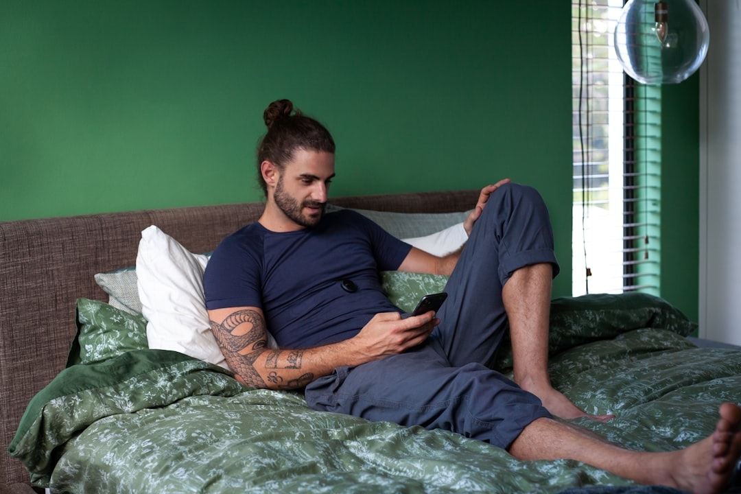 a man sitting on a bed looking at his cell phone