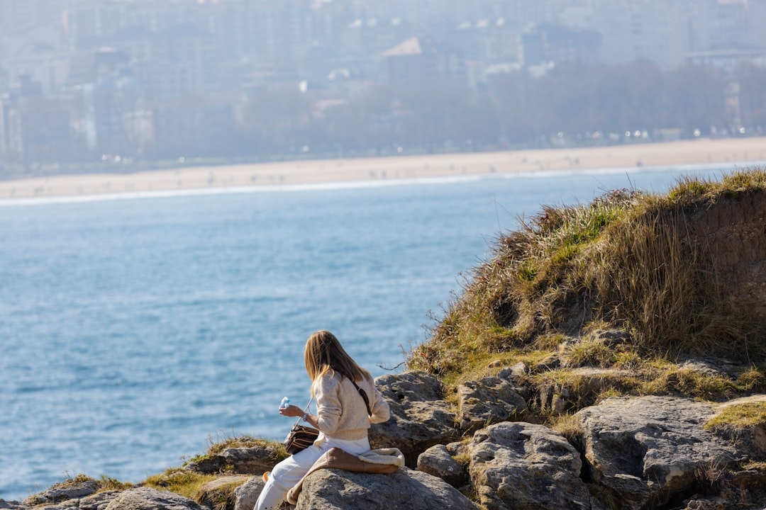 a woman sitting on a rock next to a body of water